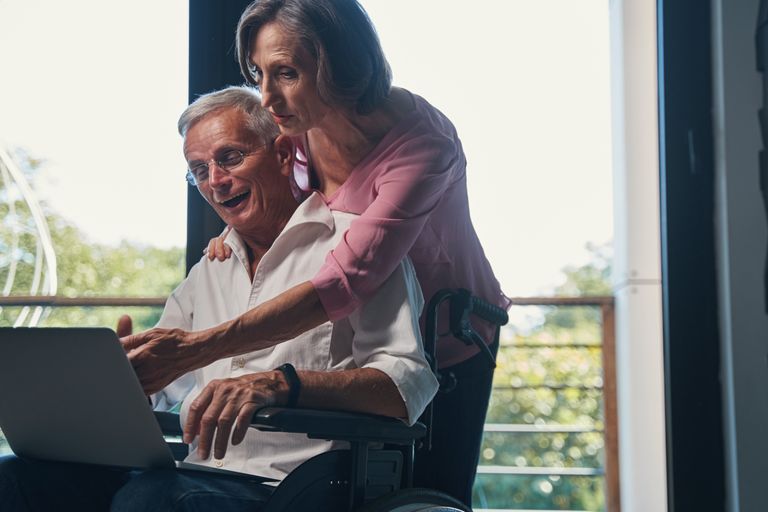 Happy senior couple using laptop together at home, woman helping man with digital tasks