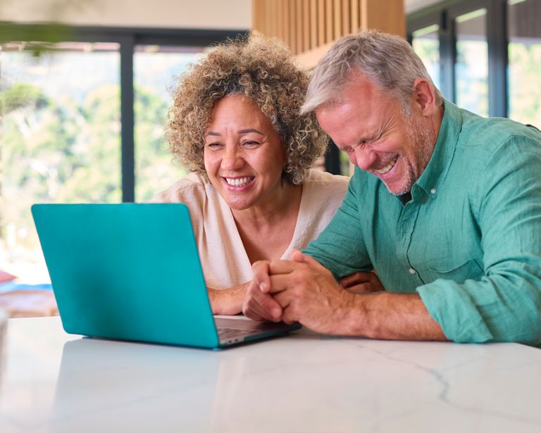 Multi-racial mature couple celebrating at home, representing independent but cautious seniors